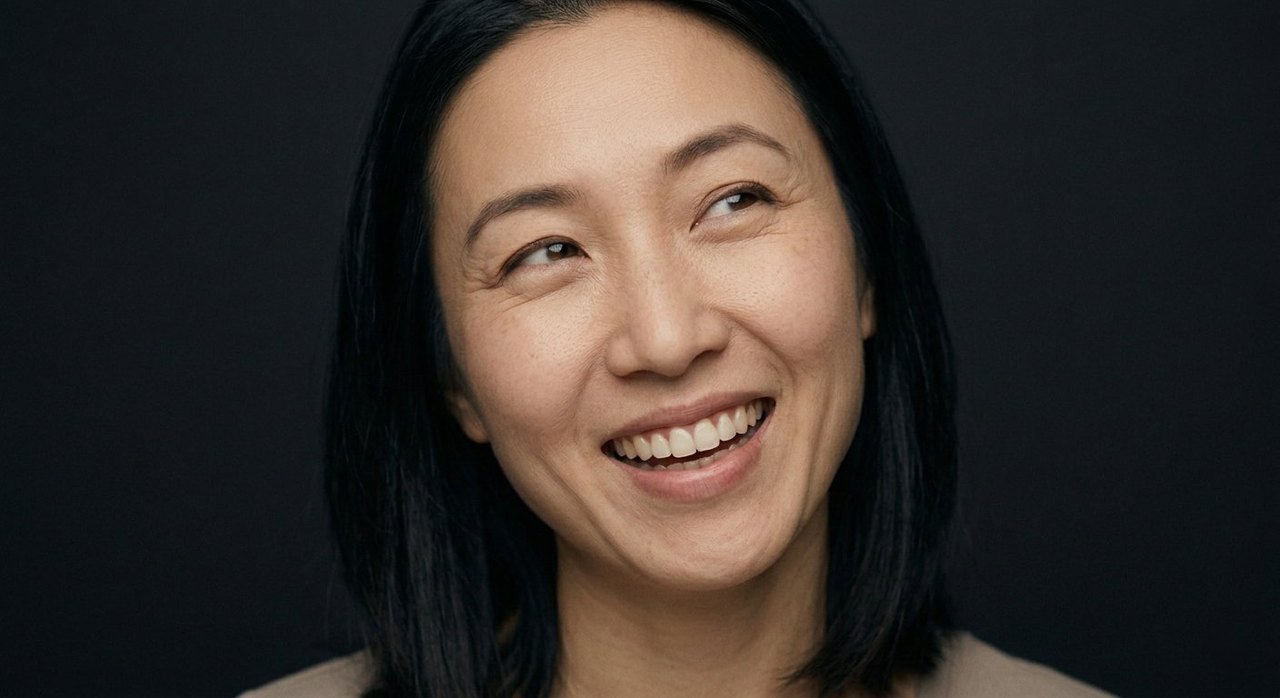 A woman's face showing amusement: an amused open smile, eyes turned aside and crinkled.