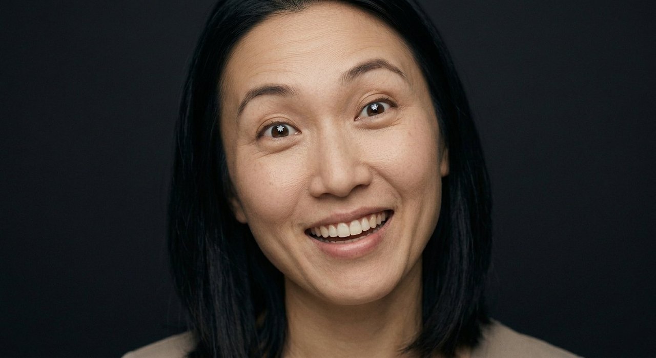 A woman's face showing delight: a bright open smile and upturned eyes, looking up.