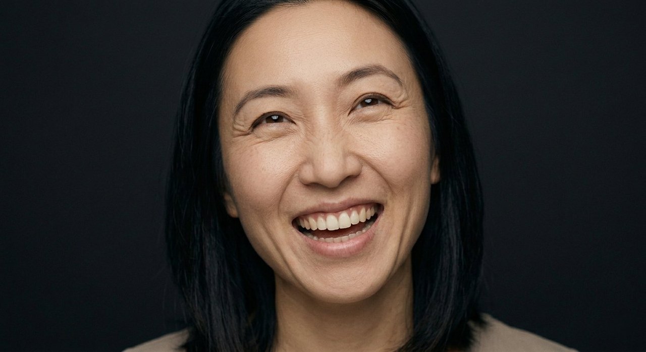 A woman's face showing exuberance: a broad joyful smile, a tilted head, lively eyes.