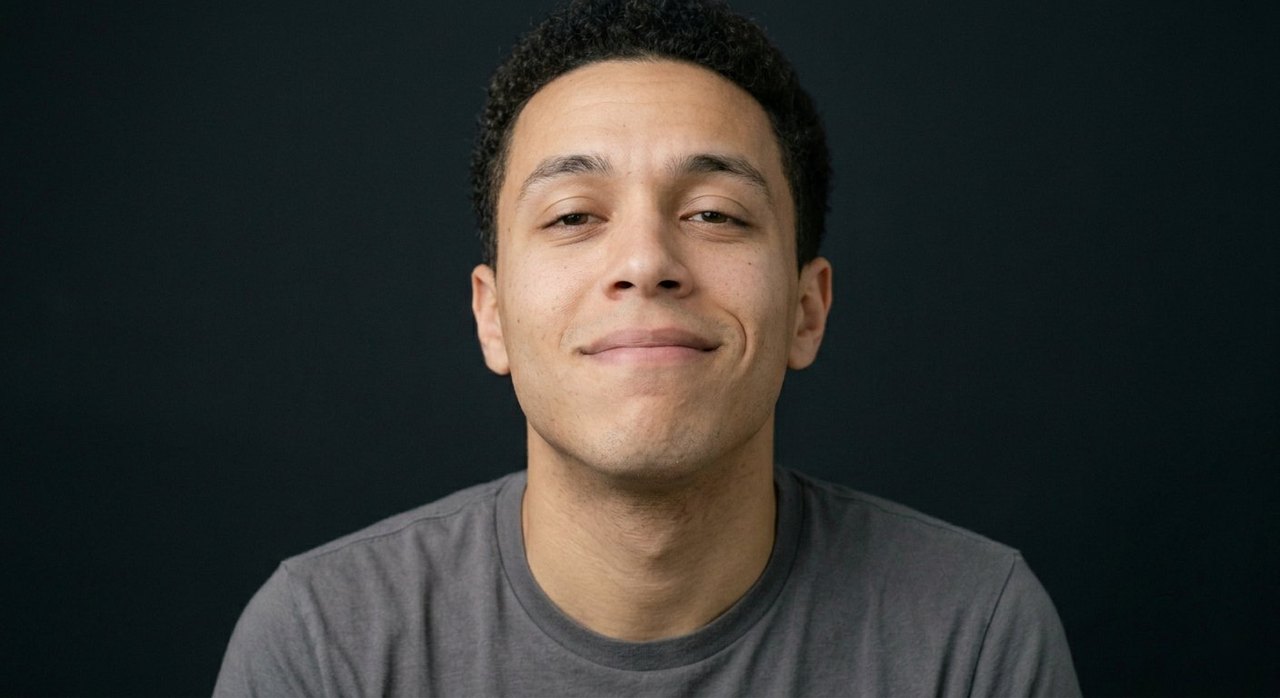 A man's face showing hubris: a smug closed smile, lifted chin, half-lidded eyes.
