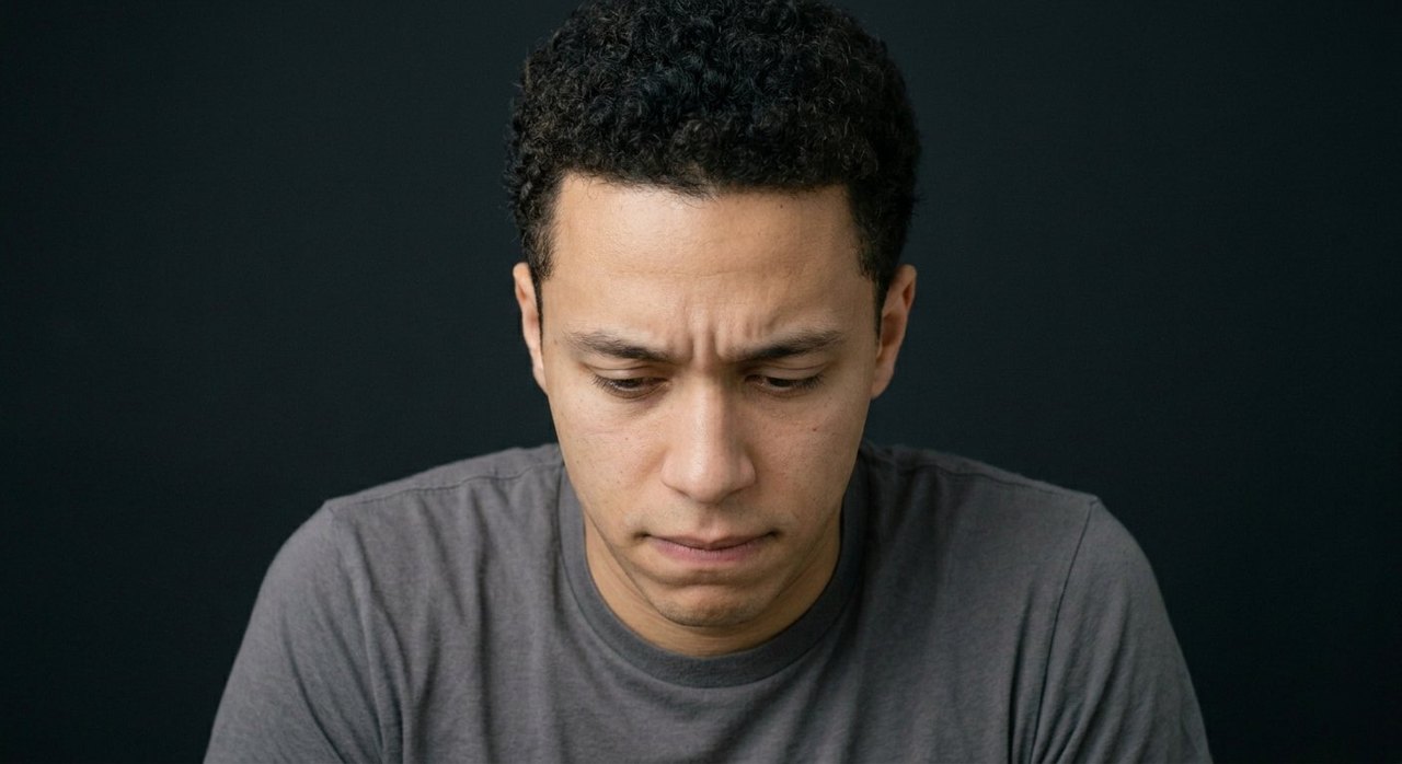 A man's face showing humiliation: head bowed low, eyes down, a tight mouth.
