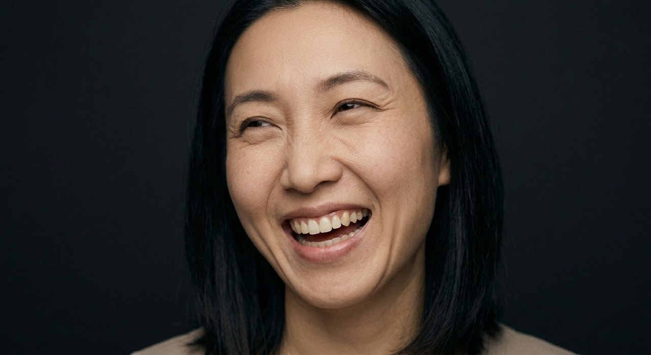 A woman's face showing mirth: an open laugh, head turned, eyes crinkled with mirth.