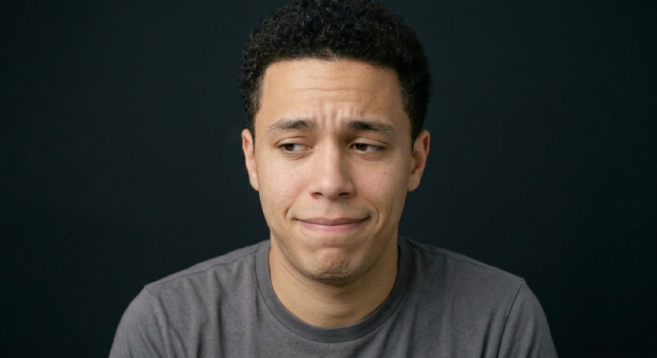 A man's face showing sheepishness: an awkward wincing half-smile, raised brow, sidelong glance.