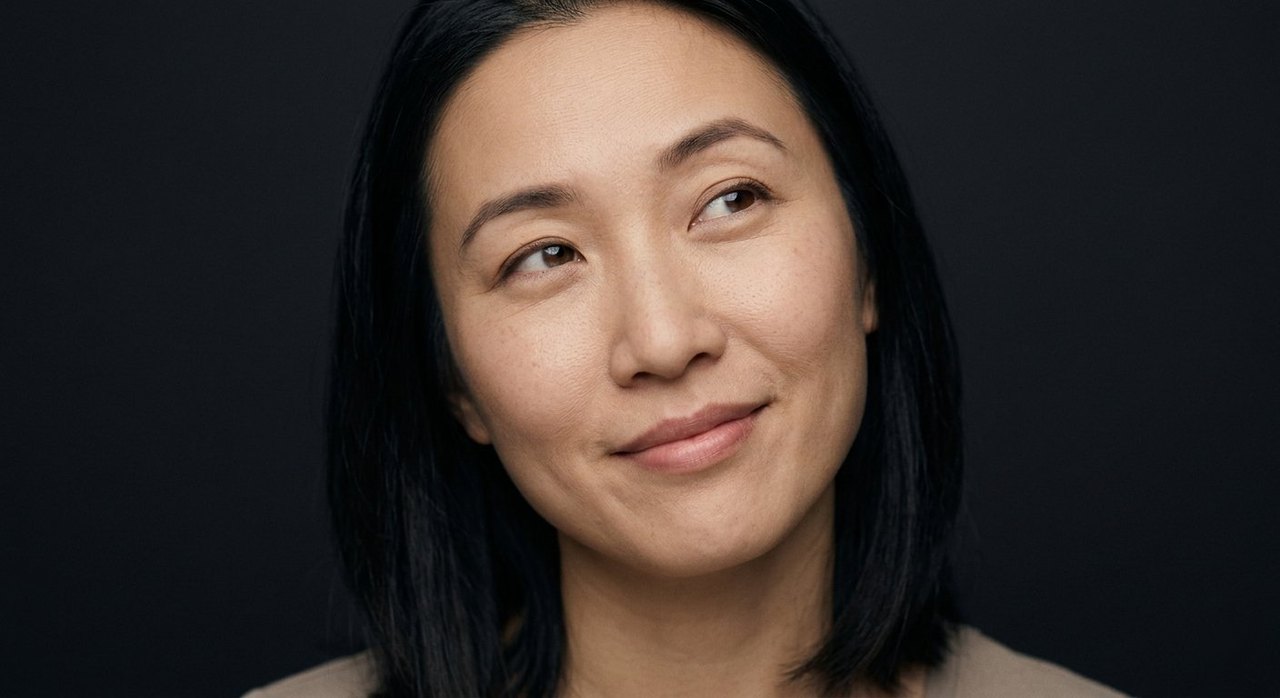 A woman's face showing whimsy: a soft amused smile, eyes drifting upward, head tilted.